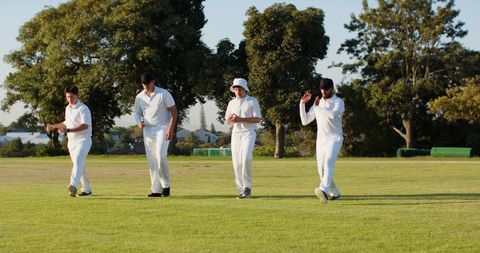 Cricket team walking across sunny suburban ground wearing white uniforms