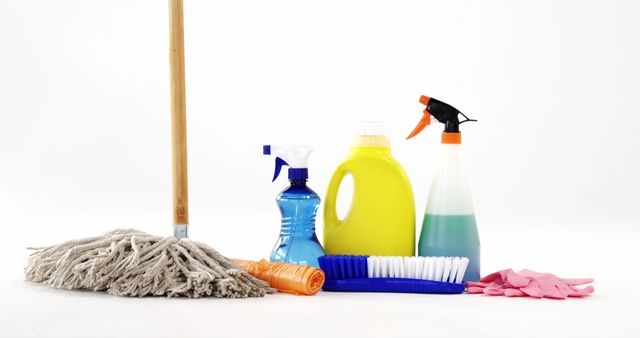 Cleaning supplies including a mop, various detergents, scrub brush, and gloves are arranged on a white background, with copy space. These items are essential for maintaining cleanliness and hygiene in residential or commercial spaces.