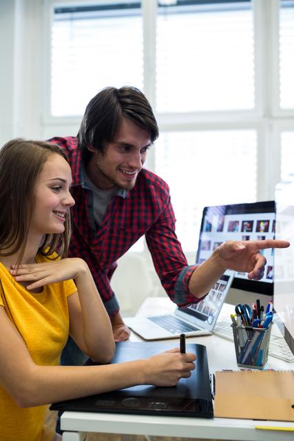 Male and female graphic designers interacting over computer in office