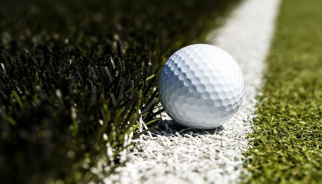 White golf ball resting on painted boundary between rough and putting green closeup