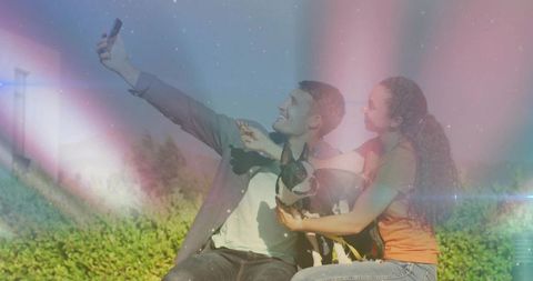 Young couple taking selfie on low park wall with boston terrier dog, pastel lens flare