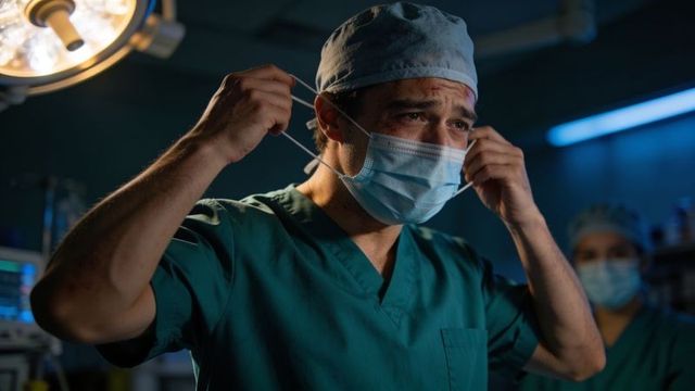 Surgeon adjusting mask in operating room showing fatigue and determination
