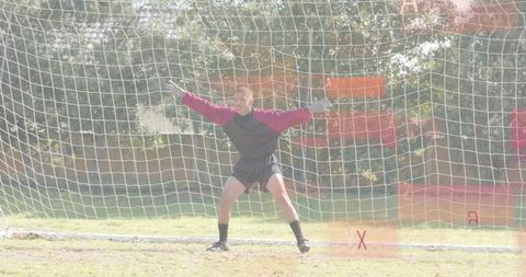 Goalkeeper bracing in net preparing for save on sunny grass field with red marking