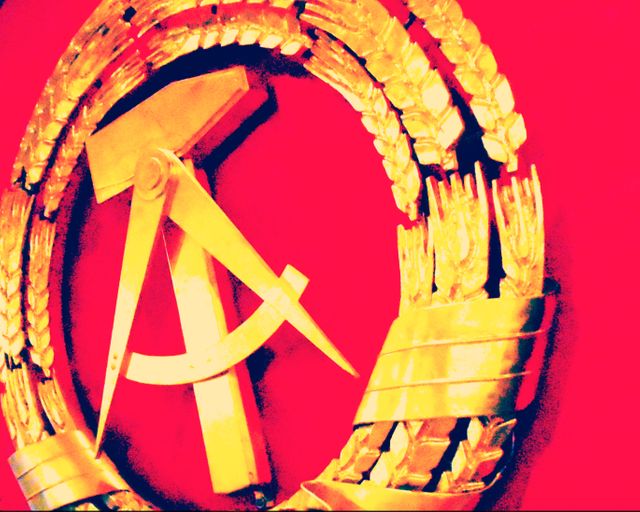 Golden emblem featuring a hammer and compass, surrounded by a wreath of wheat on a vibrant red background. This design can be used for historical articles, educational content on communism or the Soviet Union, vintage decorations, and art-related projects.