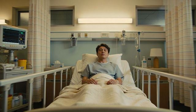 Male patient resting in hospital bed with vital signs monitor, iv stand, raised bed rails