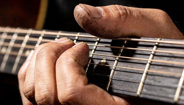 Callused fingers pressing steel strings on acoustic guitar neck closeup for rustic music