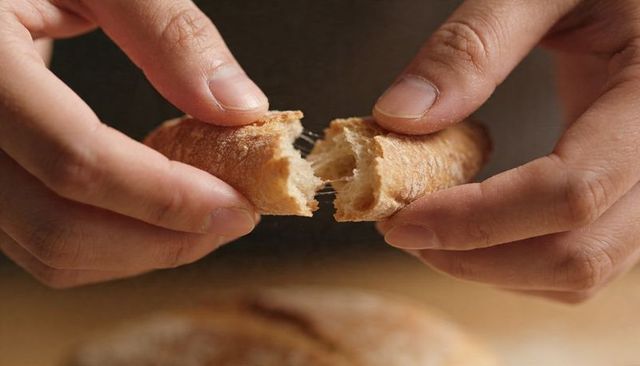 Hands tearing crusty bread roll pulling apart revealing chewy interior and rustic crumbs closeup