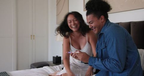 Playful Couple Laughing on Bed in Cozy Bedroom Setting