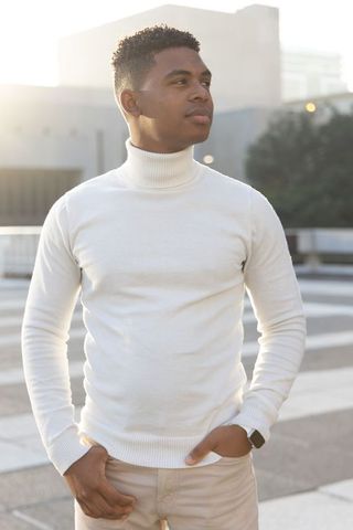 African american man standing on urban rooftop wearing white turtleneck at golden hour