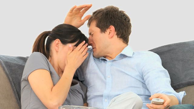 Couple sitting on sofa reacting to a scary movie on television. She is covering face in fear, while he appears anxious and protective, holding remote. Video is ideal for use in themes of home entertainment, bonding activities, movie night, or portraying emotion and reactions to media.