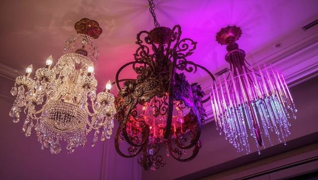 Triad of ornate crystal chandeliers casting jewel-toned light over ballroom ceiling