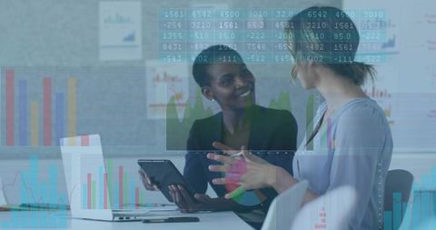 Black and white businesswomen analyzing data on tablet during collaborative office meeting