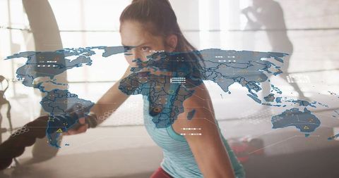 Athletic woman swinging battle ropes in boxing gym with world map hud overlay, backlit
