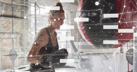Female athlete training with boxing bag under augmented reality overlay in industrial gym