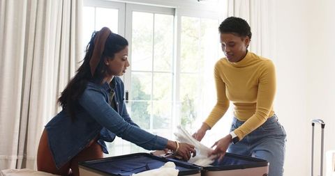 Two Women Packing Suitcase for Travel Near Sunny Window