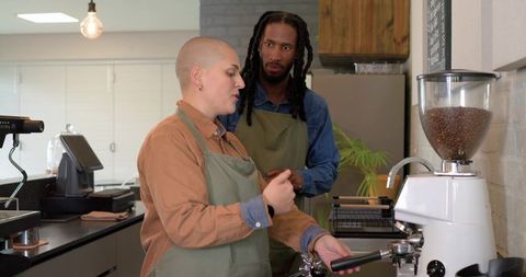 Baristas collaborating during espresso training at modern cafe counter with grinder