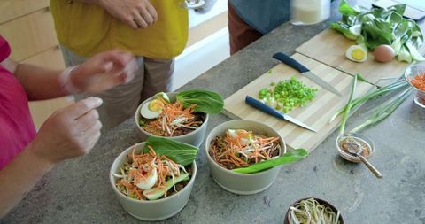 Diverse friends assembling colorful noodle bowls with fresh veggies and soft-boiled eggs
