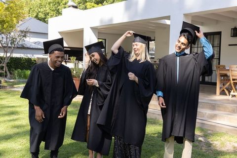 Diverse graduates celebrating together outdoors in academic attire
