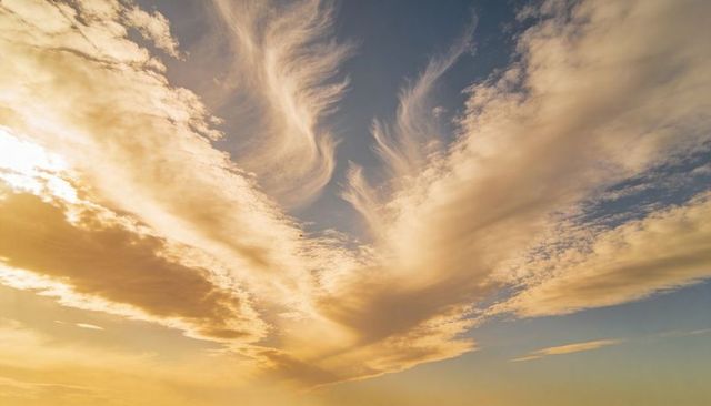 Fanning v-shaped cloud formation dominating sky at sunrise with golden glow and blue gradient
