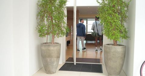 Two men walking through modern entryway flanked by large planters carrying duffel
