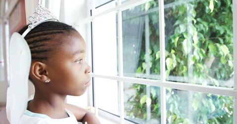 Thoughtful girl in fairy costume looking out window at home