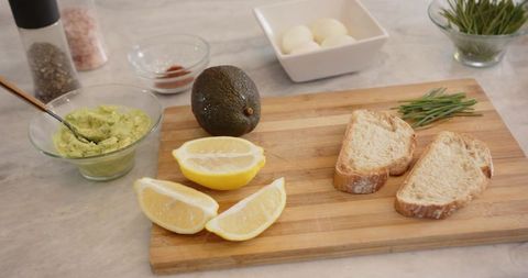 Preparing avocado toast ingredients on wooden cutting board with lemons and chives