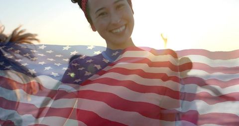 Smiling woman holding large american flag on beach at sunset backlit patriotic banner