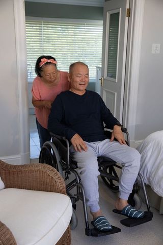 Asian senior couple in bedroom with wheelchair showing caregiving, mobility and companionship