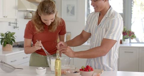 Diverse couple mixing ingredients in home kitchen for fruit dessert