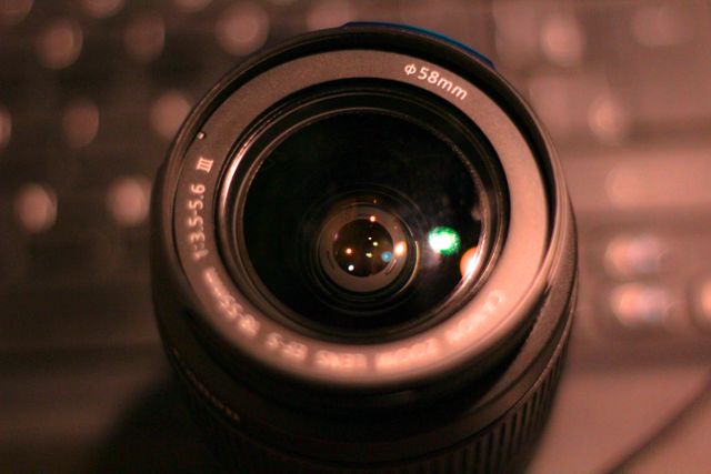 Close-up view of a camera lens with a 58mm filter, showcasing detailed glass and reflections in dim lighting. Perfect for use in articles about photography, camera equipment, lens specifications, or technical reviews. Suitable for blog posts, educational content, or professional gear advertisements.