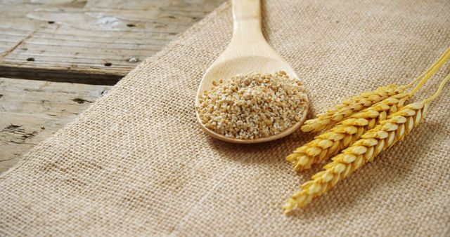 A wooden spoon filled with grains rests on a burlap surface, with stalks of wheat lying next to it, with copy space. It represents ingredients used in cooking and baking, emphasizing the importance of whole grains in a healthy diet.