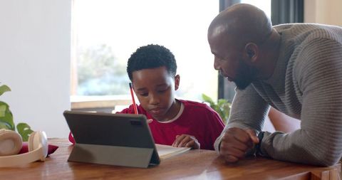 African American father mentoring son studying at home with tablet notebook and pencil