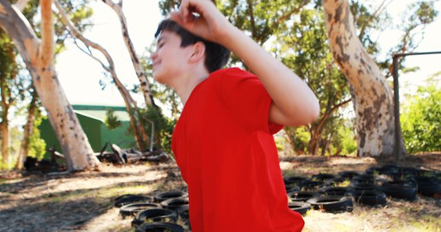 Child enjoying a sunny day outside, surrounded by trees and nature, wearing a bright red shirt. Ideal for use in materials related to outdoor activities, childhood fun, nature exploration, or summer camp advertisements.