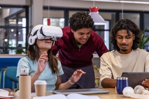 Multicultural team testing VR headset while collaborating on tablet in coworking hub