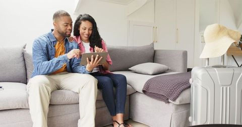 Couple Exploring Travel Options on Tablet with Packed Suitcase
