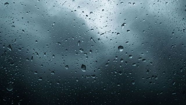 Raindrops clinging to vehicle window, misty hills looming in moody blue-gray light