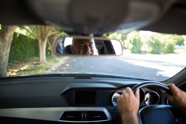 Senior man driving car with his reflection visible in the rear view mirror. Ideal for use in articles or advertisements related to senior drivers, road safety, transportation, travel, and mature lifestyle.