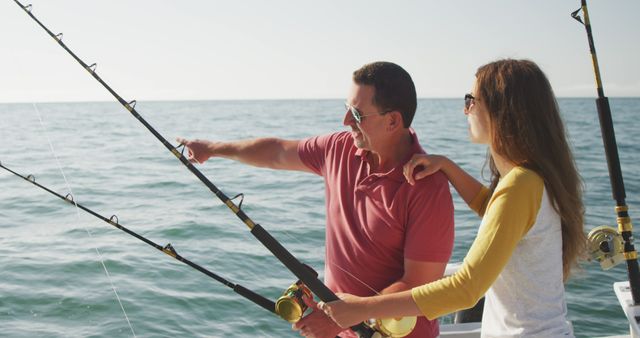 Happy caucasian father and teenage daughter fishing and talking on deck of a boat on a sunny day. Leisure, hobbies, free time, family, travel and vacations.