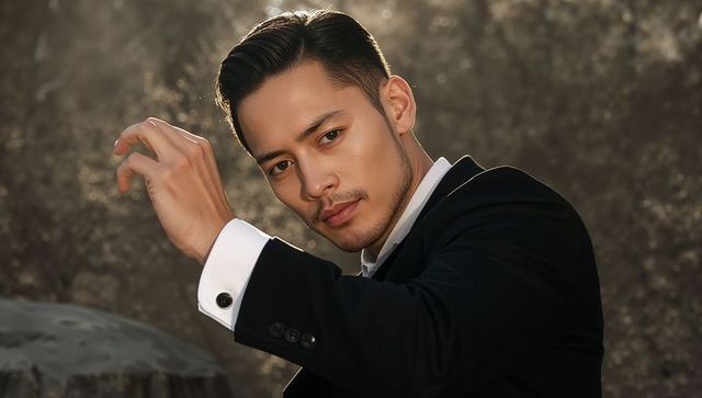 Confident asian businessman raising hand in black suit with cufflinks at golden hour headshot