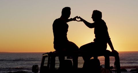 Romantic Gay Couple Creating Heart Hand Gesture at Sunset Beach
