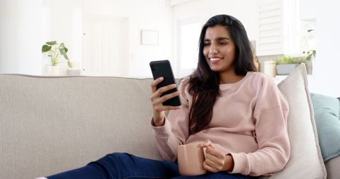 Relaxed Woman Enjoying Smartphone Time with Coffee Mug on Sofa
