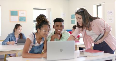 Diverse Teenagers Collaborating with Teacher on Laptop in Bright Classroom
