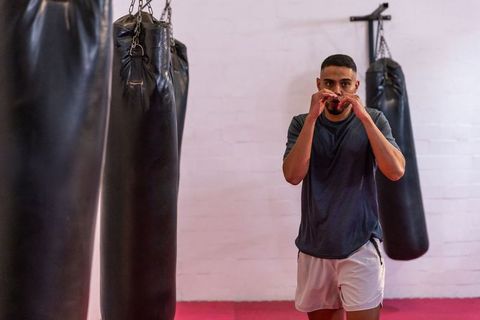 Male boxer holding guard near heavy punching bags in boxing gym training session