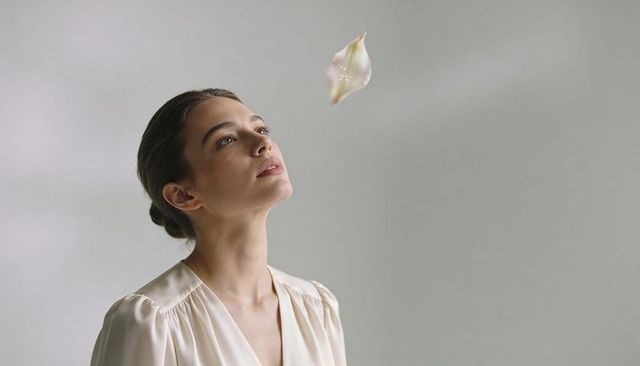 Serene woman gazing upward in cream silk blouse with floating translucent petal