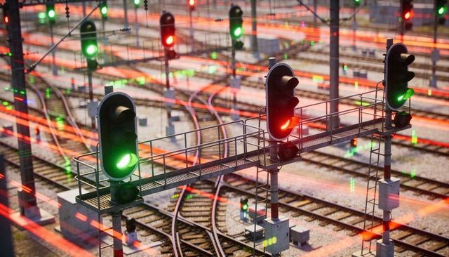 Railway signal gantry with red and green lights guiding tracks at dusk with light trails
