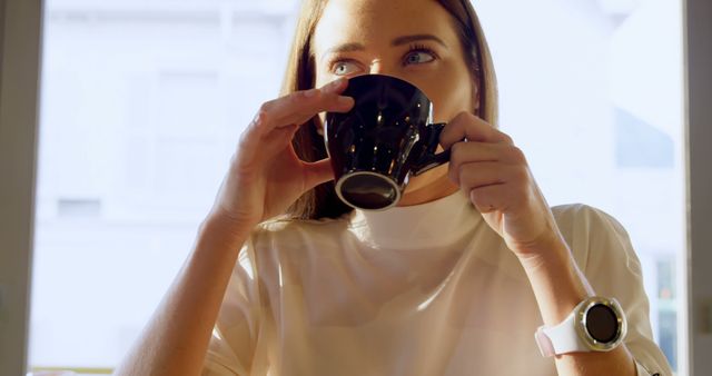A young Caucasian woman enjoys a cup of coffee in a brightly lit room, with copy space - Download Free Stock Photos Pikwizard.com