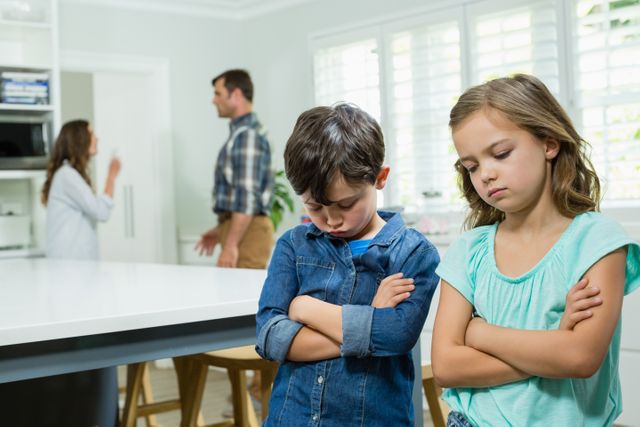 Sad siblings standing with arms crossed while parents arguing in background at home