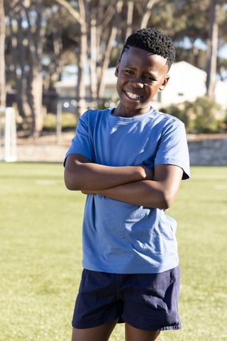 Confident african american boy posing on soccer field smiling with arms crossed