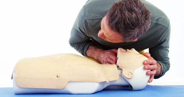 A middle-aged man is practicing CPR on a training mannequin, simulating a life-saving procedure. Such training is crucial for emergency response and equips individuals with the skills to potentially save lives in critical situations.