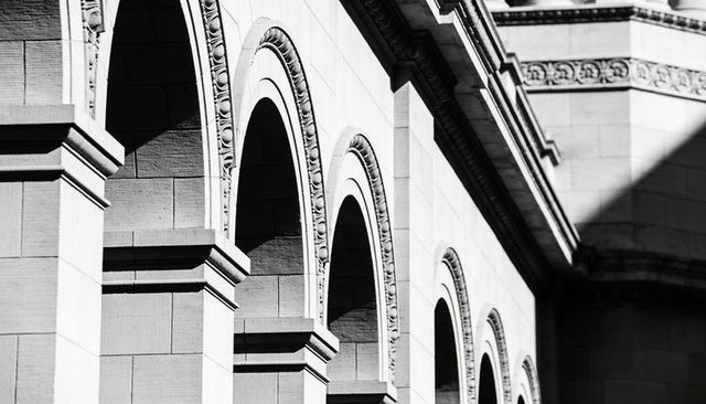Sunlight casting deep shadows across stone arches receding along classical facade